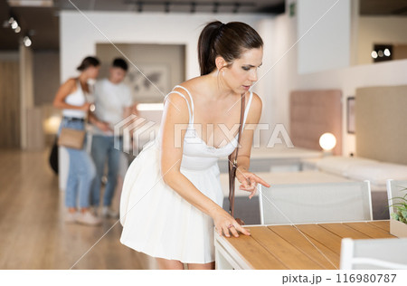 Young woman choosing convenient table in furniture shop Young woman choosing convenient table in furniture shop 116980787