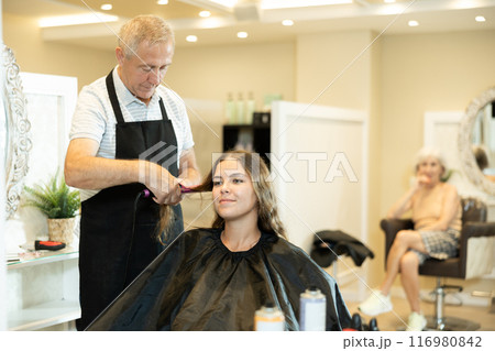 Experienced hairdresser using curling irons to create curls to young girl 116980842