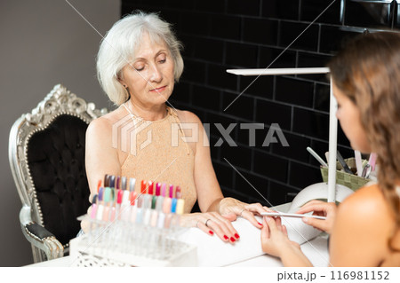 Smiling elderly woman receiving manicure from female manicurist in salon 116981152