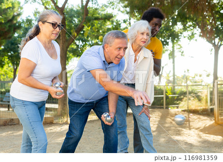 Cheerful males and females playing petanque in park on holidays Cheerful males and females playing petanque in park on holidays 116981359