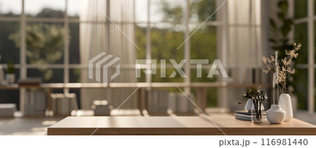 A wooden table in a contemporary Scandinavian room with sunlight streaming through a large window. 116981440