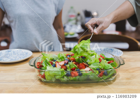 Hand with fork taking fresh vegetable and fruit salad in a plate. 116983209