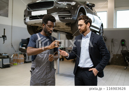Mechanic discussing vehicle repair details with customer in auto workshop Mechanic discussing vehicle repair details with customer in auto workshop 116983626