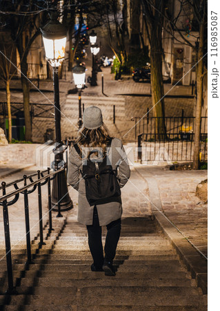 A lone woman figure descends the illuminated staircase of Montmartre under the soft glow of street lamps in Paris at night. France A lone woman figure descends the illuminated staircase of Montmartre under the soft glow of street lamps in Paris at night. France 116985087