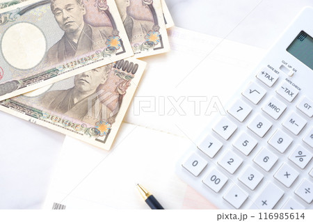 テーブルの上に開いた状態で置かれた銀行の預金通帳と、1万円札、電卓 116985614