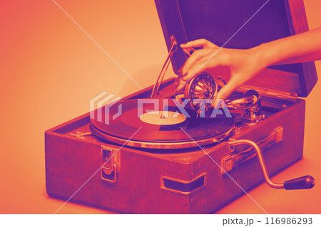 Old portable gramophone with female handA vintage gramophone, bathed in warm hues 116986293