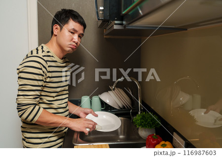 tired man washing dishes in the sink in kitchen at home 116987603