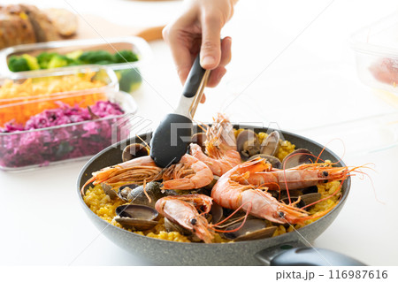 トングを使ってパエリアにエビを盛り付ける トングを使ってパエリアにエビを盛り付ける 116987616