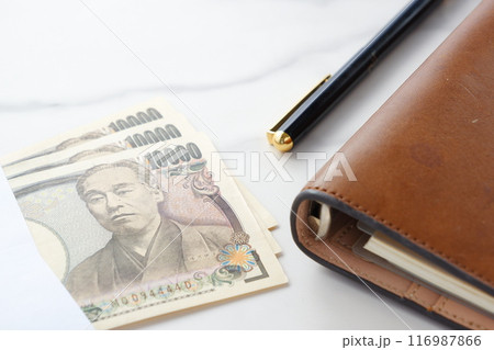 福沢諭吉の肖像の一万円紙幣と、茶色の革の手帳 福沢諭吉の肖像の一万円紙幣と、茶色の革の手帳 116987866