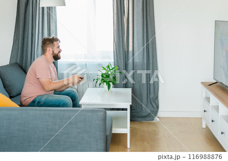 Man playing video games in living room sitting on sofa. Man playing video games in living room sitting on sofa. 116988876