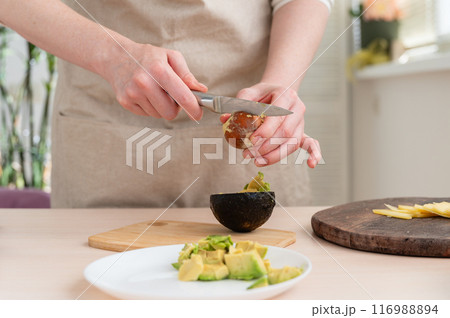 Woman cutting fresh avocado in kitchen. Close-up. 116988894