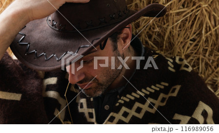 Tired cowboy leaning on hay bale 116989056