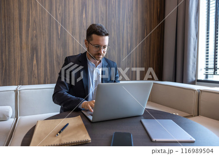 Confident businessman in glasses working on laptop computer in office interior 116989504
