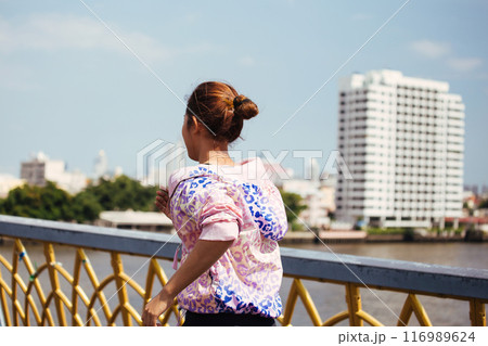 Back view of Asian female in sportswear running near railing of bridge over river during outdoor workout on city street Back view of Asian female in sportswear running near railing of bridge over river during outdoor workout on city street 116989624
