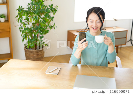 コーヒー片手にスマホを見るミドル女性 116990071