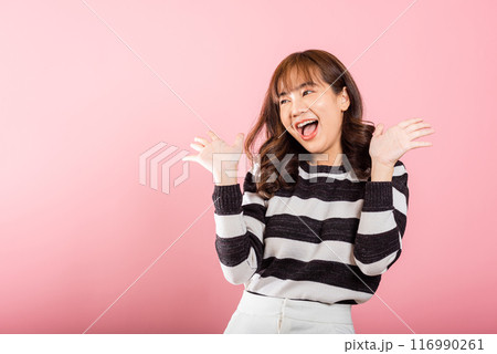 A jubilant woman raises her fists in celebration of her success, saying yes with excitement. Asian portrait of a happy young female in a studio shot on a pink background. A jubilant woman raises her fists in celebration of her success, saying yes with excitement. Asian portrait of a happy young female in a studio shot on a pink background. 116990261