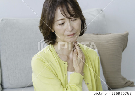 リビングに座る肩を抑えるミドルエイジの女性 116990763