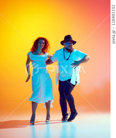 Couple dancers rehearses with energy, focusing on fluid movements and rhythmic precision in neon light against gradient orange background. Couple dancers rehearses with energy, focusing on fluid movements and rhythmic precision in neon light against gradient orange background. 116991332
