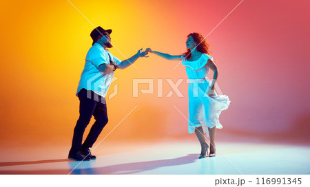 Dancers work on precise coordination and timing in neon light against gradient orange background. Love Latin dance. Dancers work on precise coordination and timing in neon light against gradient orange background. Love Latin dance. 116991345