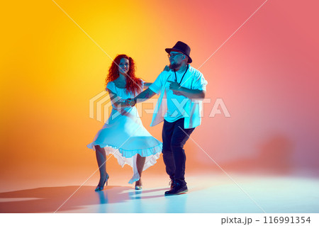 Focused on salsa training, dance couple work on precision and fluidity during practice session in neon light against gradient orange background. 116991354