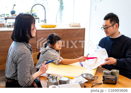 ハザードマップを見ながら家族が集まる場所をマジックで指している娘とマップを持ちながら見守る夫婦 116993606