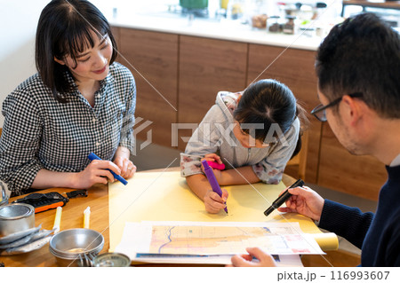 もしも被災して家族がバラバラになった時に集合する場所を大きな神に記入している娘とそれを見守る夫婦 116993607