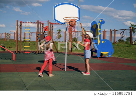 Little girls play basketball on an outdoor summer playground, clearly throwing ball into the basket Little girls play basketball on an outdoor summer playground, clearly throwing ball into the basket 116993781