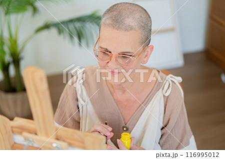 Senior Woman with Shaved Head Painting in a Bright, Modern Studio with Natural Light Senior Woman with Shaved Head Painting in a Bright, Modern Studio with Natural Light 116995012