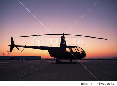 A black helicopter is sitting on the ground at sunset. 116995013