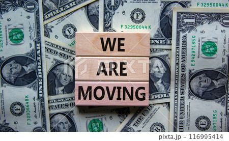 We are moving symbol. Wooden blocks with words 'We are moving'. Beautiful background from dollar bills. Business, we are moving concept, copy space. We are moving symbol. Wooden blocks with words 'We are moving'. Beautiful background from dollar bills. Business, we are moving concept, copy space. 116995414