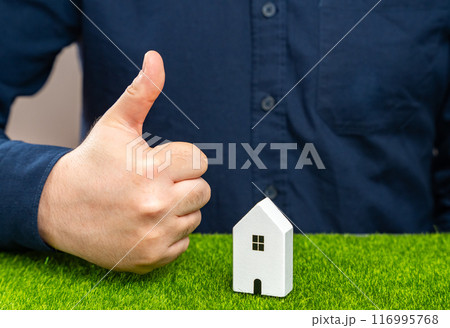 A man shows a thumbs up near a house. Successful real estate investment. Completion of a favorable deal. Approval of a mortgage or loan, making the purchase or renovation possible. Approves condition 116995768
