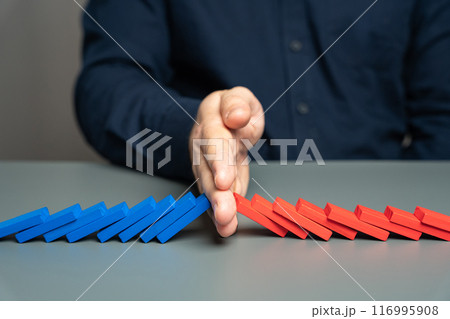A man stops two domino chains from colliding. The concept of stopping a conflict and preventing further escalation. Elections and confrontation of the parties. Mentoring. Find points of compromise. A man stops two domino chains from colliding. The concept of stopping a conflict and preventing further escalation. Elections and confrontation of the parties. Mentoring. Find points of compromise. 116995908