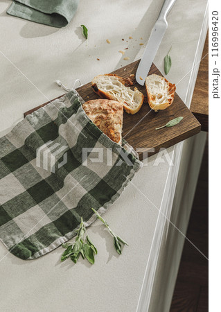 Sliced bread in linen bag on wooden board, fresh herbs and stainless still kitchen knife. Kitchen aesthetic concept Sliced bread in linen bag on wooden board, fresh herbs and stainless still kitchen knife. Kitchen aesthetic concept 116996420