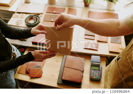 High angle shot of female and male hands holding small paper bag with leather goods 116996864
