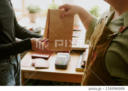 Medium close up of cashier giving paper bag to consumer 116996866