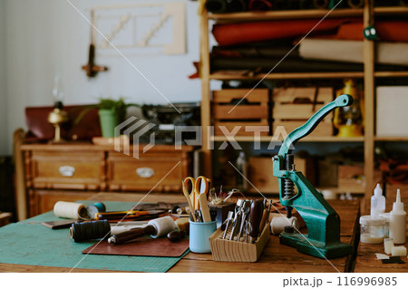 Turquoise leather punch machine with sewing tools on old wooden table in atelier Turquoise leather punch machine with sewing tools on old wooden table in atelier 116996985