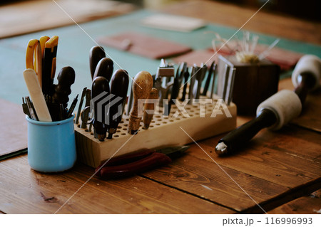 Medium close up of leather punches, awl and scissors on wooden table 116996993