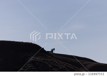 Silhouetted Figures Trekking Atop a Serene Hillside at Dusk 116997531