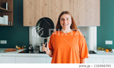 Young woman housewife holding empty pan in the kitchen at home. Domestic life and diet concept. Food banner. Time to eat 116998765