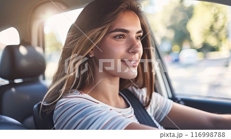 A young woman with a serene expression, driving a car, with sunlight streaming through the window 116998788