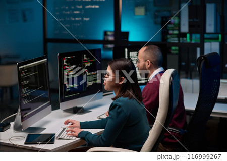 High angle view at two people sitting at workplace in cybersecurity department and writing code in blue lights 116999267