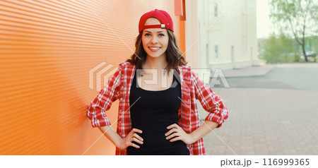Summer portrait of happy smiling young woman posing in red baseball cap, casual clothes 116999365