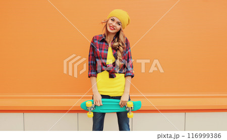 Stylish happy young blonde woman posing with skateboard on city street 116999386