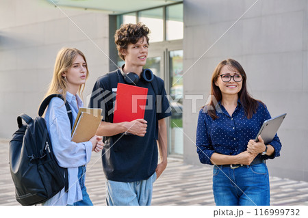 Group of college students talking with female teacher, educational building background Group of college students talking with female teacher, educational building background 116999732
