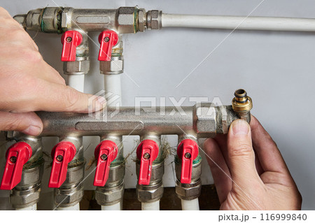 Plumber installing manifold for plastic pipes with five outlets. 116999840