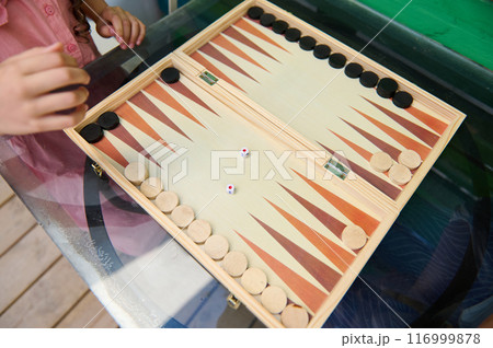 Child playing backgammon with wooden pieces on a glass table outdoors 116999878