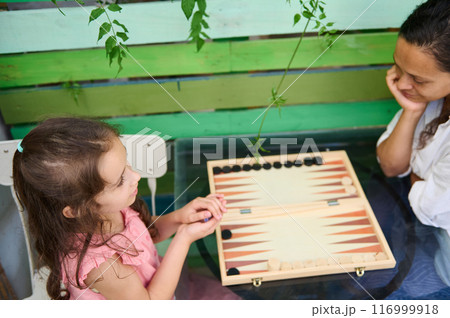 Mother and daughter bond over backgammon game at home. Family and leisure time together 116999918