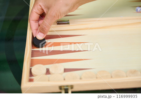 Hand placing chip in backgammon game on wooden board Hand placing chip in backgammon game on wooden board 116999935