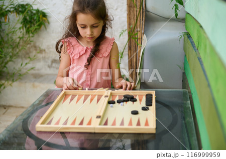 Young girl playing backgammon outdoors on a glass table Young girl playing backgammon outdoors on a glass table 116999959
