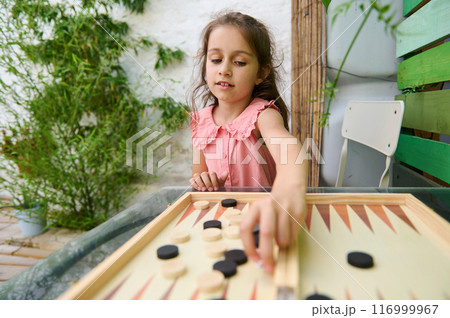 Young girl playing backgammon in a garden setting on a sunny day Young girl playing backgammon in a garden setting on a sunny day 116999967